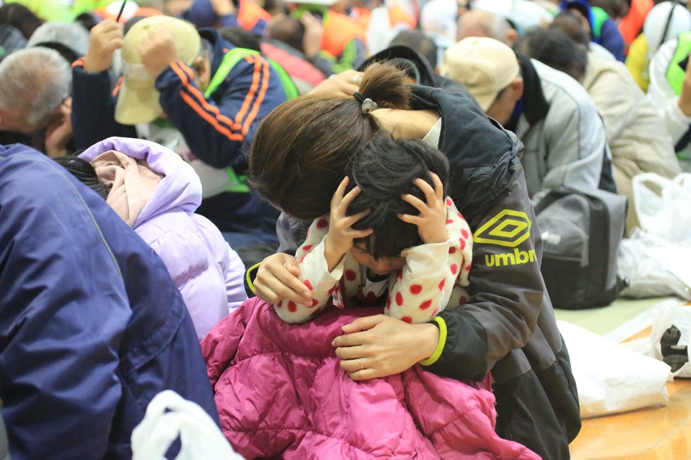 写真:緊急地震速報対応訓練にて頭部を守る参加者 緊急地震速報対応訓練.JPG
